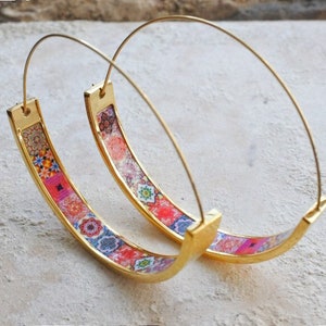 May include: A pair of gold hoop earrings with a colorful patterned design. The pattern features a variety of geometric shapes and colors, including pink, blue, and green.