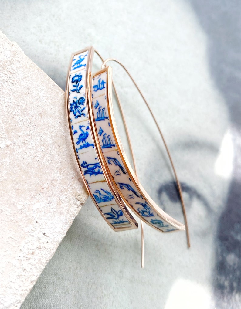 Op de afbeelding: Een paar gouden creolen met een wit en blauw patroon. Het patroon bevat vogels, bloemen en geometrische vormen.