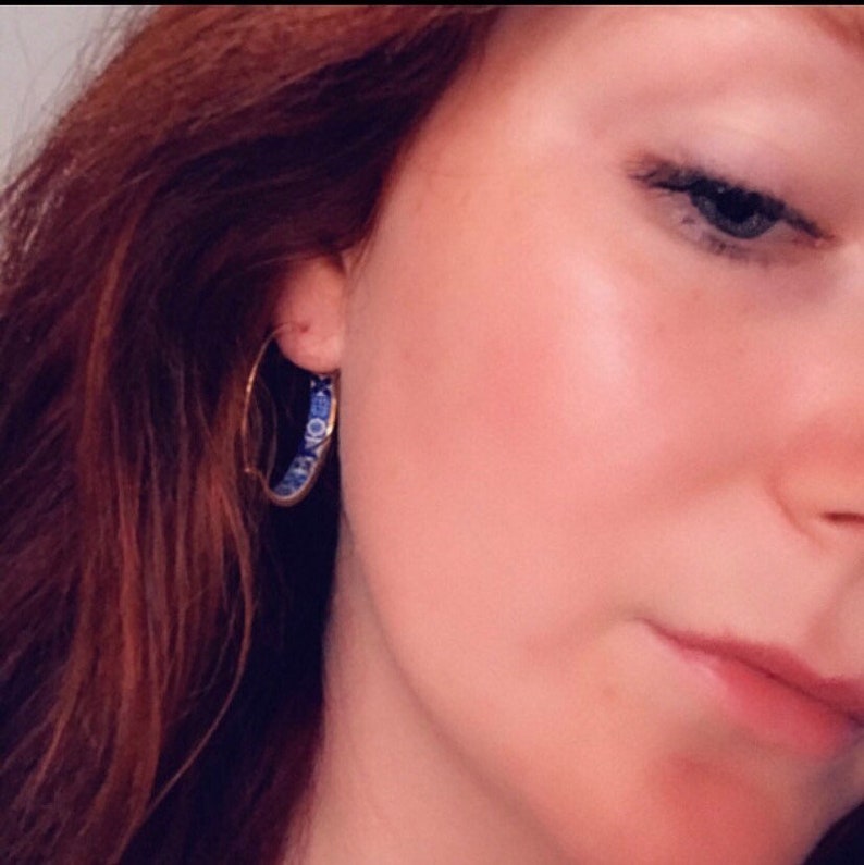 May include: A pair of gold hoop earrings with a blue and white patterned design.