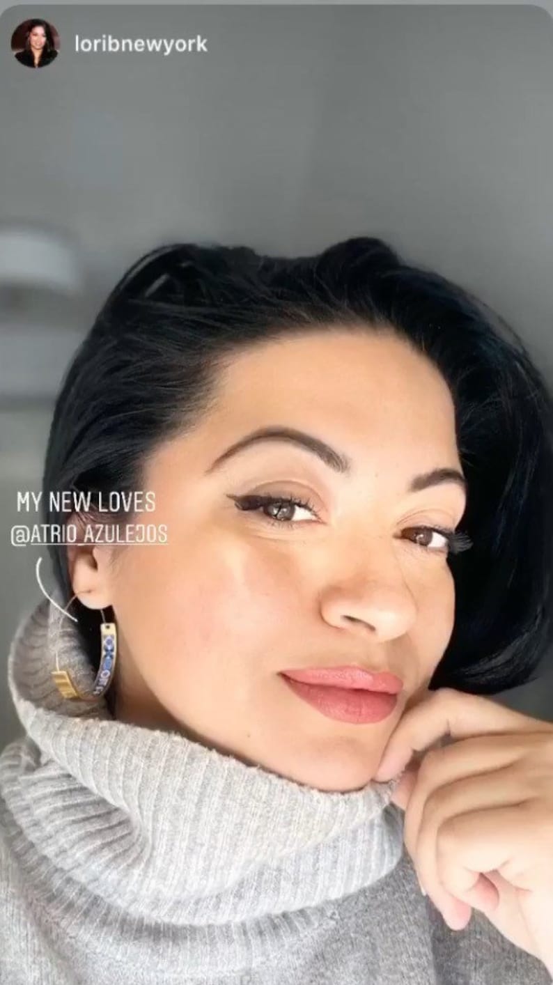 May include: A woman with dark hair wearing a gray turtleneck sweater and gold hoop earrings with blue and white accents. The text "MY NEW LOVES @ATRIOAZULEJOS" is visible in the image.
