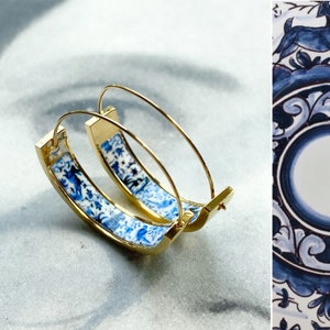 Könnte beinhalten: Goldene Creolen mit einem blauen und weißen Porzellan-Design. Das Design zeigt ein Blumenmuster und einen Vogel.