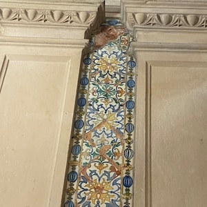May include: A close-up of a wall with a decorative tile strip. The tile strip is made of white, blue, green, and yellow tiles with a floral pattern. The tiles are arranged in a vertical pattern.