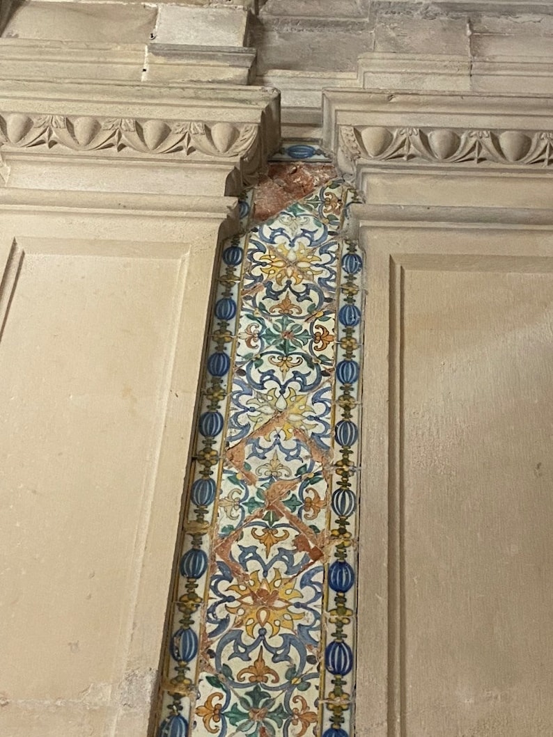 May include: A close-up of a wall with a decorative tile strip. The tile strip is made of white, blue, green, and yellow tiles with a floral pattern. The tiles are arranged in a vertical pattern.