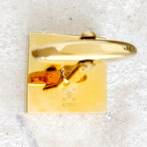 May include: Gold square cufflinks with a starburst design and the word "&Aacute;TRIO" engraved on the front.