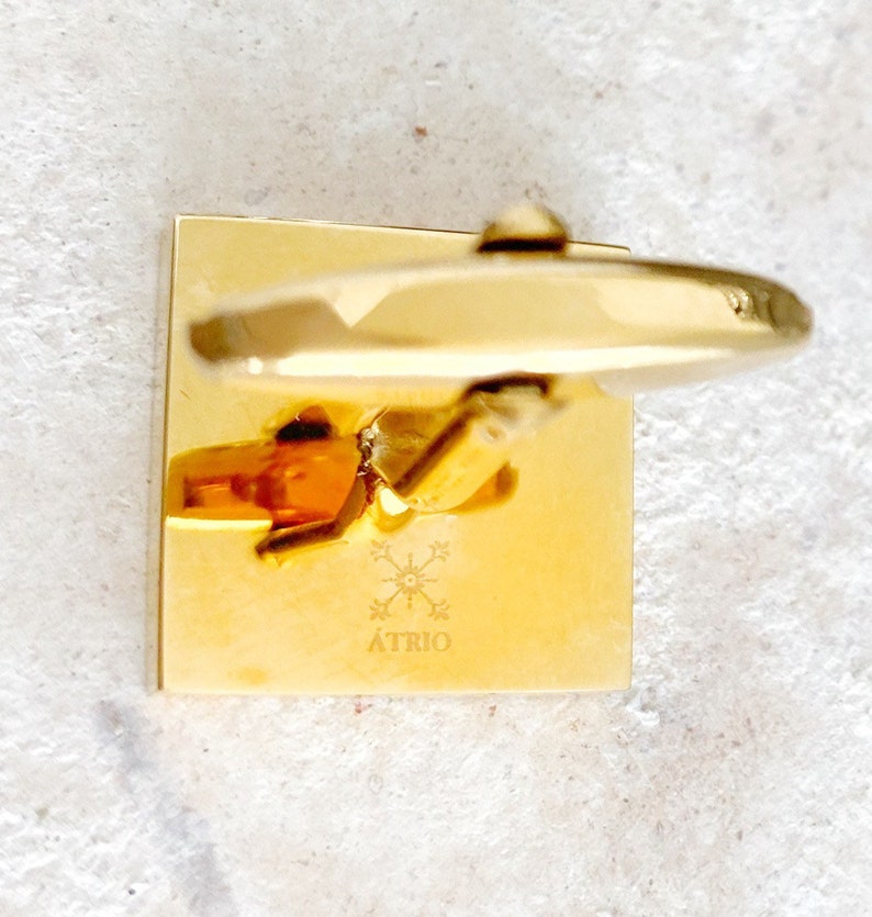 May include: Gold square cufflinks with a starburst design and the word "&Aacute;TRIO" engraved on the front.
