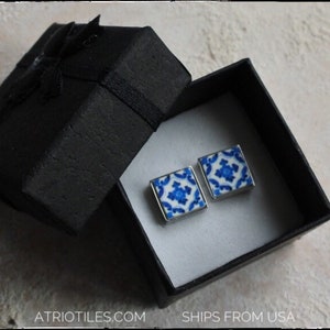 May include: A pair of blue and white ceramic tile earrings in a black gift box. The earrings are square shaped and feature a geometric pattern.