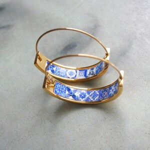 May include: Gold hoop earrings with a blue and white patterned design. The pattern is reminiscent of traditional Portuguese tiles.
