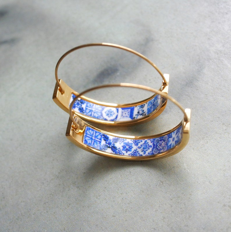 May include: Gold hoop earrings with a blue and white patterned design. The pattern is reminiscent of traditional Portuguese tiles.