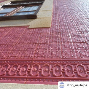 May include: A close-up of a wall covered in red tiles with a repeating floral pattern. The tiles are arranged in a grid pattern and have a slightly raised texture. The wall is angled upwards, creating a perspective effect. The tiles are a deep red color, and the floral pattern is a lighter shade of red. The tiles are a traditional Portuguese style, known as azulejos.