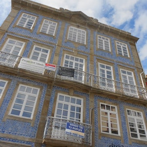 May include: A building with blue and white tiled accents. The building has multiple windows and a sign that reads "VENDO T83 T3 DUPLEX 910 795 356".