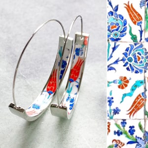 May include: A pair of silver hoop earrings with a white background and a colorful floral pattern. The pattern features red, blue, and green flowers and leaves.