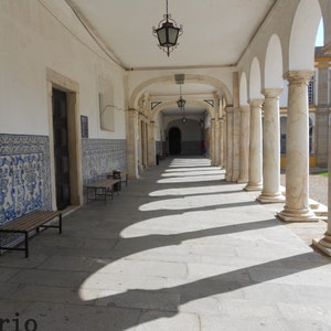 Peut inclure: Un b&acirc;timent blanc avec une longue all&eacute;e couverte bord&eacute;e de colonnes blanches. L'all&eacute;e est carrel&eacute;e et a un mur carrel&eacute; bleu et blanc sur le c&ocirc;t&eacute; gauche. Le texte "Atrio" est visible sur le sol.