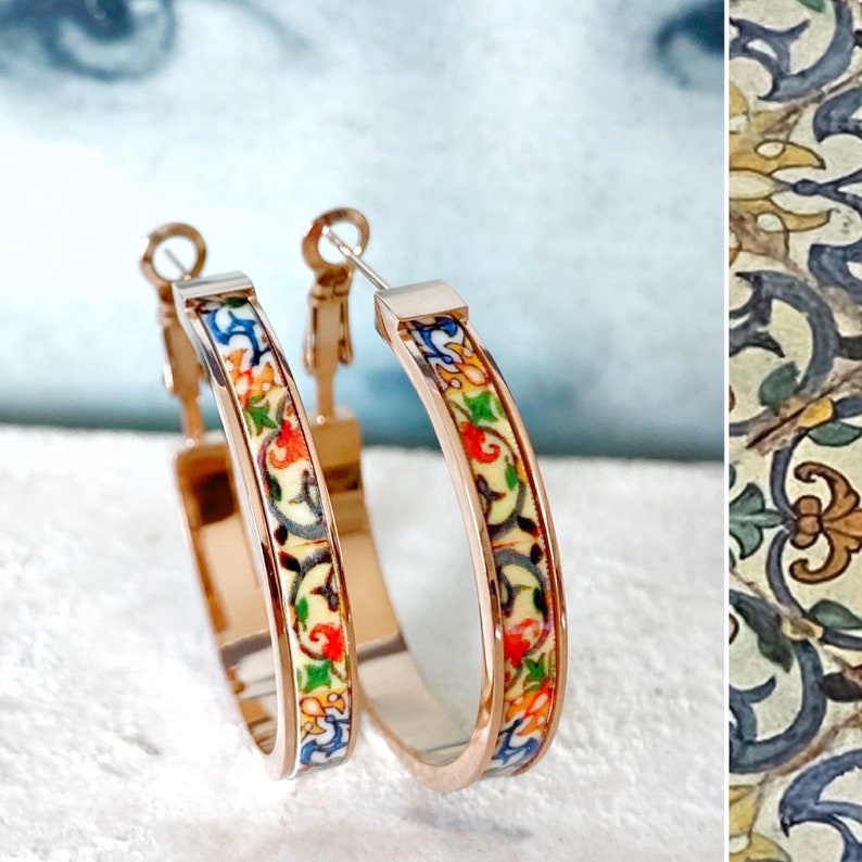 May include: A pair of gold hoop earrings with a colorful floral pattern. The pattern is reminiscent of traditional Spanish tile designs.