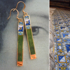 May include: A pair of gold earrings with green and blue tile-like designs. The earrings are rectangular and have a gold hook closure.