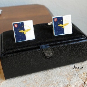 Puede incluir: Una caja de cuero negro con un par de gemelos con la bandera de las Azores. Los gemelos son de plata con un dise&ntilde;o de bandera azul y blanca con un &aacute;guila amarilla.