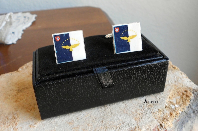 Puede incluir: Una caja de cuero negro con un par de gemelos con la bandera de las Azores. Los gemelos son de plata con un dise&ntilde;o de bandera azul y blanca con un &aacute;guila amarilla.