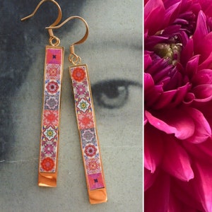 May include: A pair of gold dangle earrings with a rectangular design. The earrings feature a colorful pattern of geometric shapes and floral motifs.