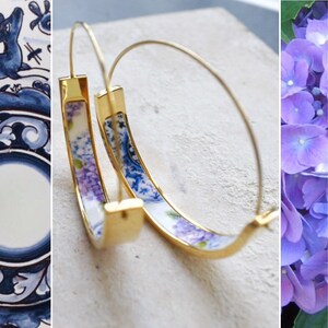 May include: A pair of gold hoop earrings with a blue and white porcelain design. The porcelain features a floral pattern with purple and white flowers.
