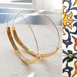 May include: Gold hoop earrings with a colorful floral pattern around the edge. The pattern is reminiscent of traditional Spanish tiles.