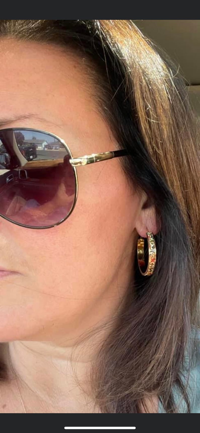 May include: A woman wearing gold hoop earrings with a textured design. She is wearing sunglasses and has long brown hair.