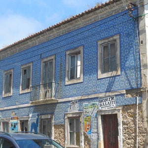 May include: A building with blue and white tiled walls and several windows. The building has a brown roof and a stone facade. There are several posters on the building, including one that says "Homem Balafi" and another that says "Nazar&eacute;".