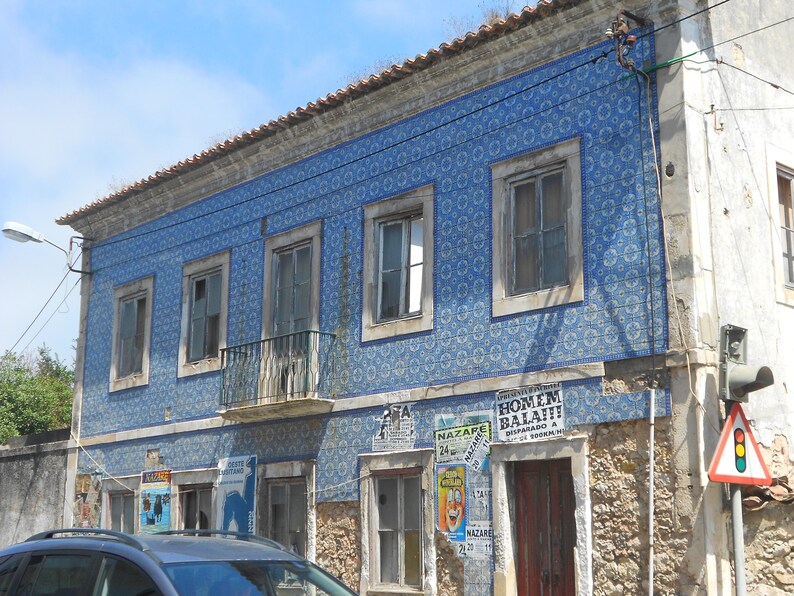 May include: A building with blue and white tiled walls and several windows. The building has a brown roof and a stone facade. There are several posters on the building, including one that says "Homem Balafi" and another that says "Nazar&eacute;".