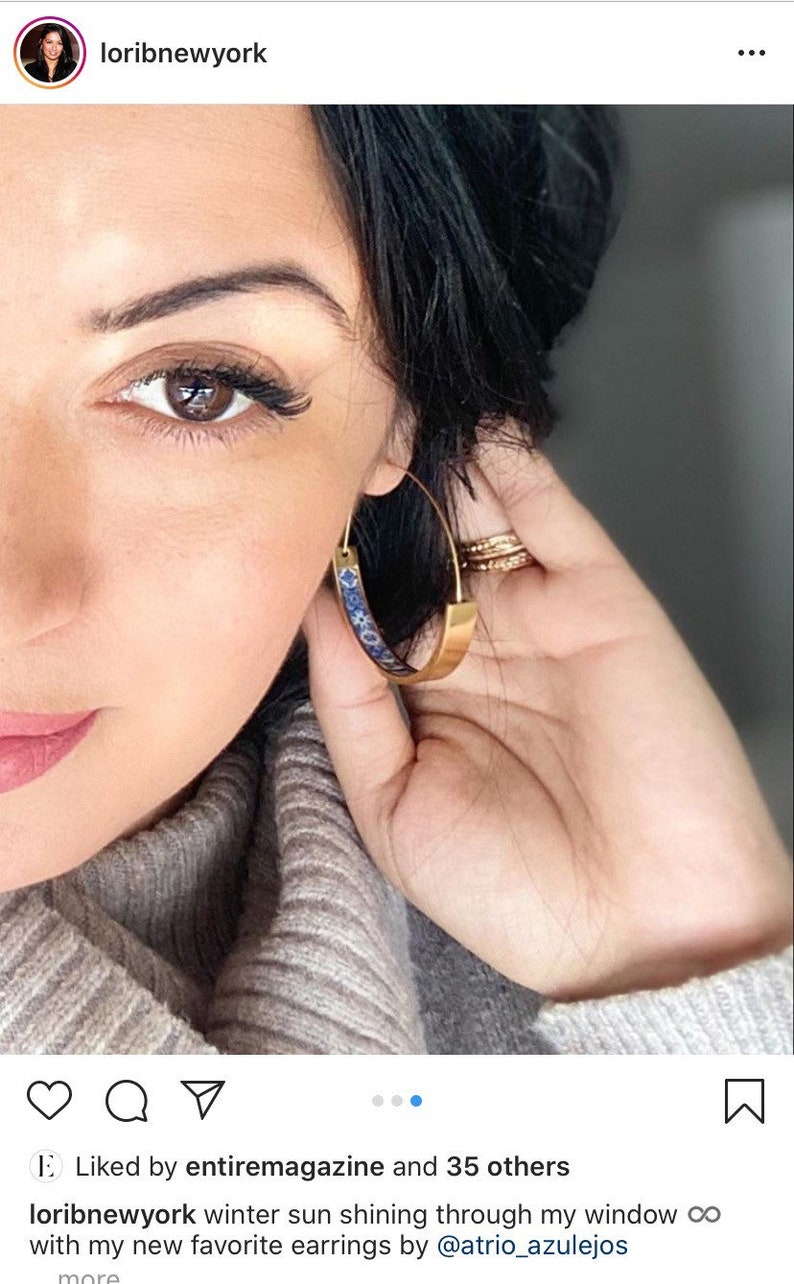 May include: Close-up of a person's face wearing gold hoop earrings with a blue and white patterned design. The earrings are large and have a wide band.