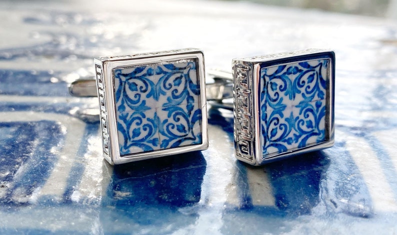 Puede incluir: Un par de gemelos de plata con un dise&ntilde;o estampado en azul y blanco. El patr&oacute;n recuerda a los azulejos portugueses tradicionales.