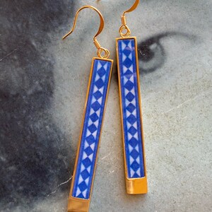 May include: A pair of gold dangle earrings with blue and white geometric patterned rectangular charms.