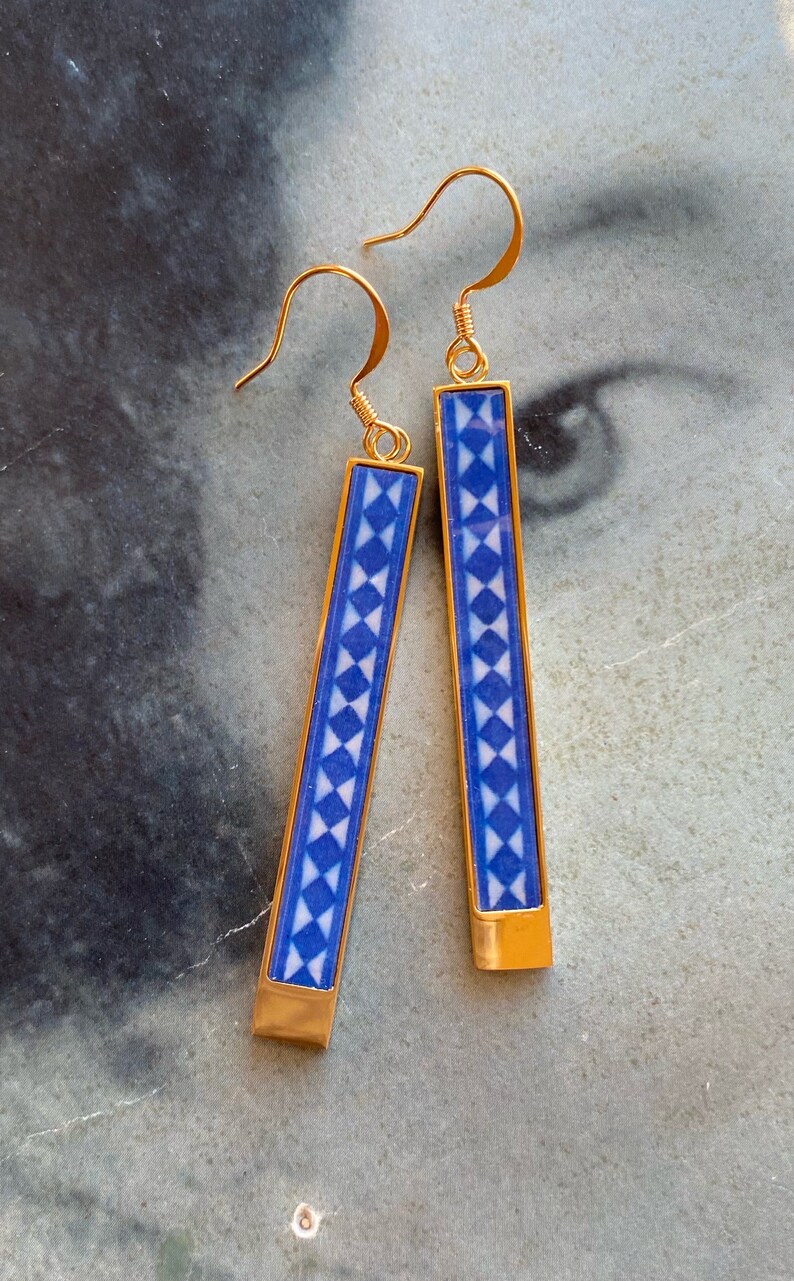 May include: A pair of gold dangle earrings with blue and white geometric patterned rectangular charms.