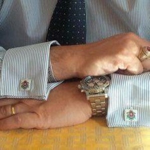 Puede incluir: Un par de gemelos de plata con un dise&ntilde;o floral rojo y blanco. Los gemelos se llevan en una camisa de rayas con un reloj de oro en la otra mu&ntilde;eca.