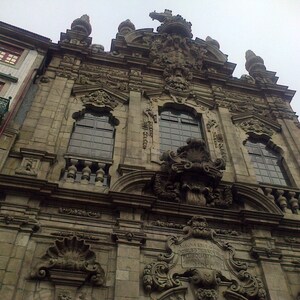 Puede incluir: Una vista detallada de un edificio de piedra con tallas intrincadas y una gran puerta arqueada. El edificio tiene un aspecto desgastado y antiguo, con una fachada de piedra gris y detalles ornamentados.