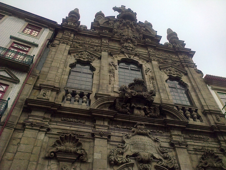 Puede incluir: Una vista detallada de un edificio de piedra con tallas intrincadas y una gran puerta arqueada. El edificio tiene un aspecto desgastado y antiguo, con una fachada de piedra gris y detalles ornamentados.