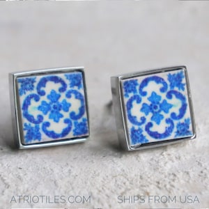 May include: A pair of silver square earrings with blue and white patterned ceramic tiles. The tiles feature a floral design.
