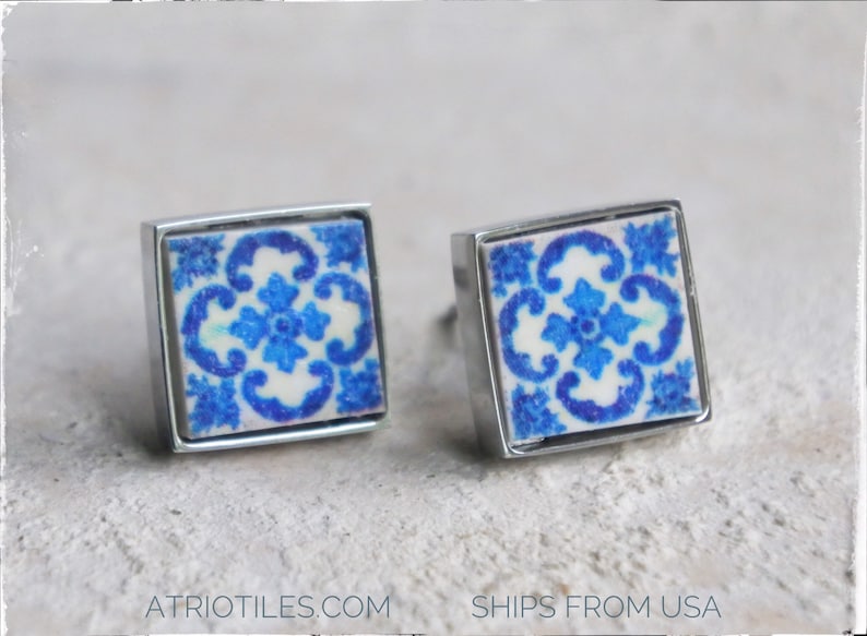 May include: A pair of silver square earrings with blue and white patterned ceramic tiles. The tiles feature a floral design.