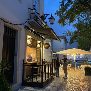 May include: A small restaurant with a wooden patio and a white awning. The restaurant is called "Bistr&ocirc; Mia". Two people are standing outside the restaurant.