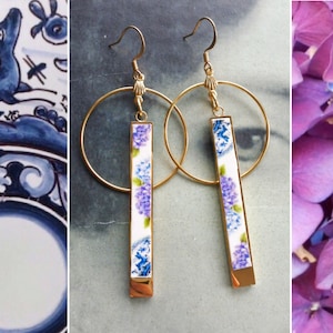 May include: A pair of gold hoop earrings with a white and blue floral design. The earrings are made of metal and have a dangling floral design.