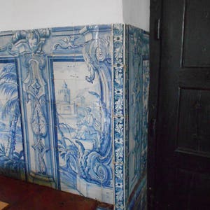 Op de afbeelding: Blauwe en witte tegelwand met een decoratief patroon. De tegels zijn in een rasterpatroon gerangschikt en hebben een verscheidenheid aan bloem- en geometrische ontwerpen. De tegels zijn geplaatst tegen een witte achtergrond.
