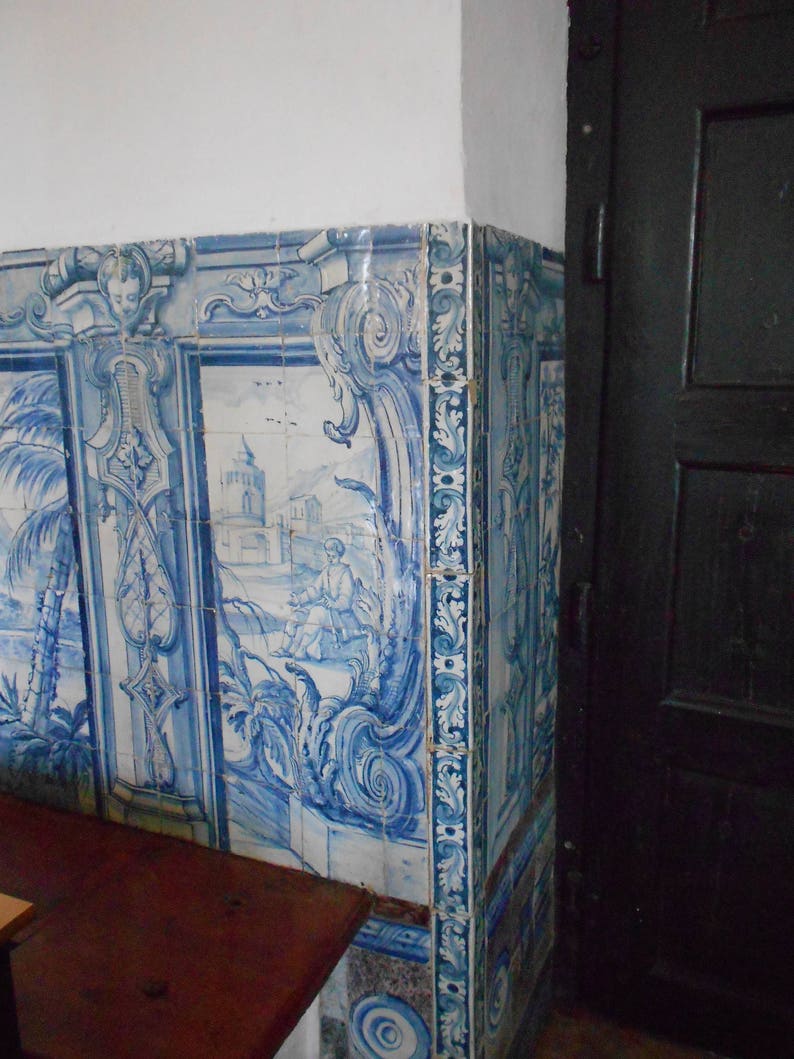 Op de afbeelding: Blauwe en witte tegelwand met een decoratief patroon. De tegels zijn in een rasterpatroon gerangschikt en hebben een verscheidenheid aan bloem- en geometrische ontwerpen. De tegels zijn geplaatst tegen een witte achtergrond.