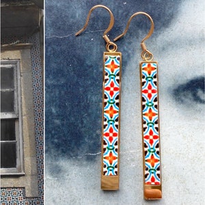 May include: A pair of gold dangle earrings with a colorful geometric pattern. The earrings are made of metal and have a rectangular shape.