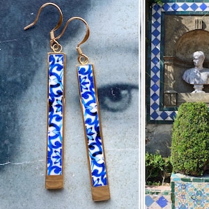 May include: A pair of gold dangle earrings with blue and white ceramic rectangular panels. The panels feature a floral pattern.