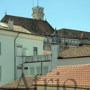 May include: A white building with a clock tower and red tile roofs. The building has multiple windows and a balcony. The clock tower has a blue clock face.