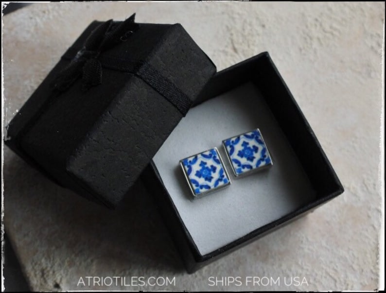 May include: A pair of blue and white ceramic tile earrings in a black gift box. The earrings are square shaped and feature a geometric pattern.