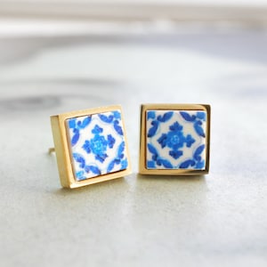 May include: A pair of gold square earrings with blue and white patterned tile insets.