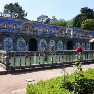 May include: A blue and white tiled fountain with a stone railing and a red rose bush in the foreground.