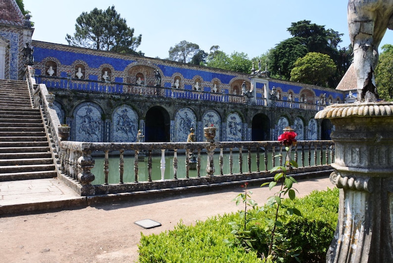 May include: A blue and white tiled fountain with a stone railing and a red rose bush in the foreground.