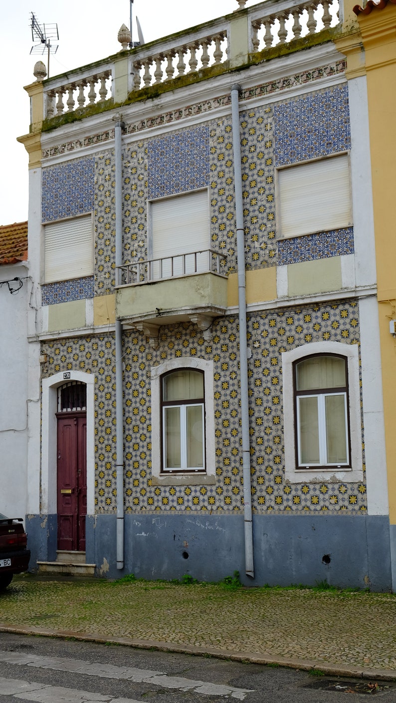 Peut inclure: Un b&acirc;timent avec une fa&ccedil;ade en carrelage. Les carreaux sont de couleur jaune et bleue. Il y a trois fen&ecirc;tres avec des volets blancs et une porte rouge. Le b&acirc;timent poss&egrave;de un balcon avec une balustrade blanche.