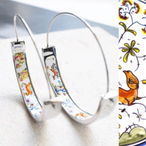 Könnte beinhalten: Ein Paar silberne Creolen mit einer weißen Porzellaneinlage, die mit einem farbenfrohen Blumen- und Tierdesign verziert ist.