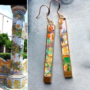 May include: A pair of gold dangle earrings with a rectangular design. The earrings feature a colorful floral pattern with orange, yellow, green, and blue accents.
