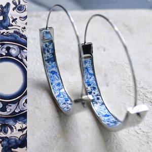 Könnte beinhalten: Ein Paar silberne Creolen mit einem blauen und weißen Porzellan-Design. Das Design zeigt ein Blumenmuster mit weißem Hintergrund und blauen Akzenten.